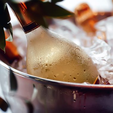Bottle of white wine sparkling in a bucket of ice, leaves, close-up, iny, droplets, condensation, bokeh, blurred background